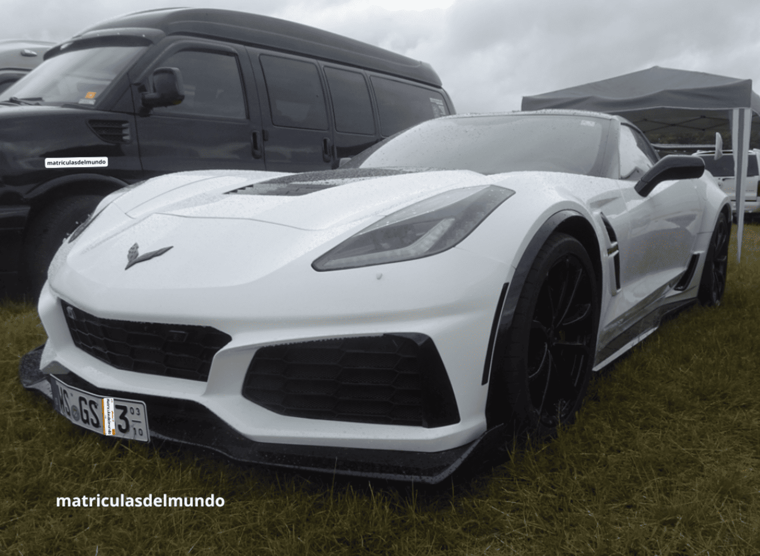 Chevrolet Corvette blanco con matrícula de temporada de Alemania en un prado y con una carpa